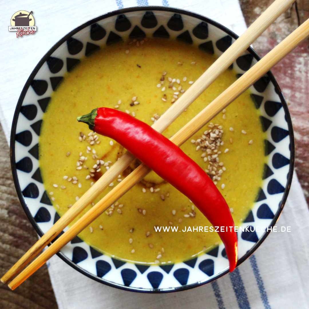 Über einer blauweißen Schale mit Pastinakensuppe liegen Essstäbchen, auf denen Chilischote angerichtet ist