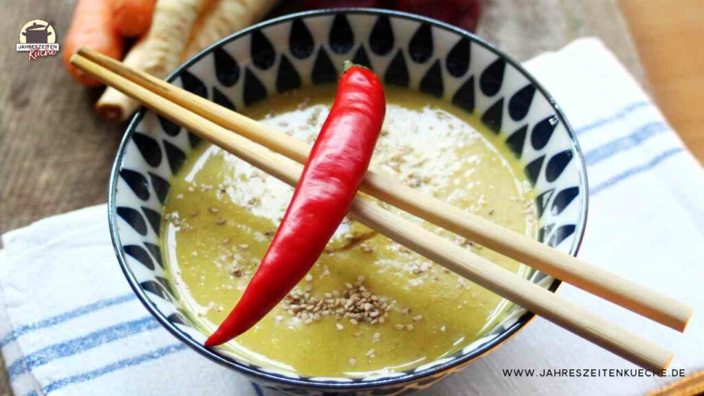 Pastinakensuppe in einer Schüssel, darüber Essstäbchen und eine Chilischote