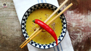 Eine Chilischote liegt auf Essstäbchen, die auf eine Schale mit Pastinakensuppe gelegt sind