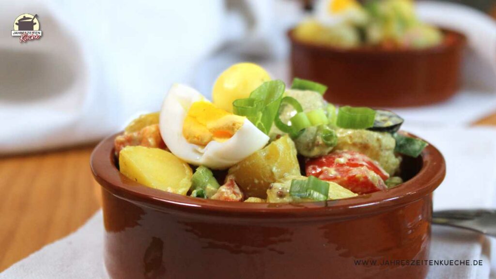 2 Steingutschalen mit Pellkartoffelsalat, auf denen ein Viertel Ei liegt.