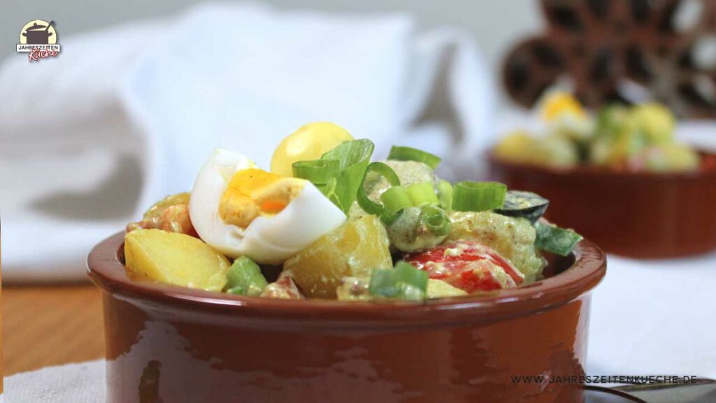 Steingutschale mit Pellkartoffelsalat, der mit Lauchzwiebeln bestreut ist.