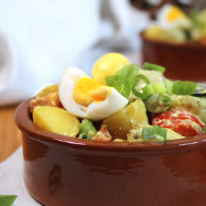 Pellkartoffelsalat mit Lauchzwiebeln bestreut in einer Steingutschale.