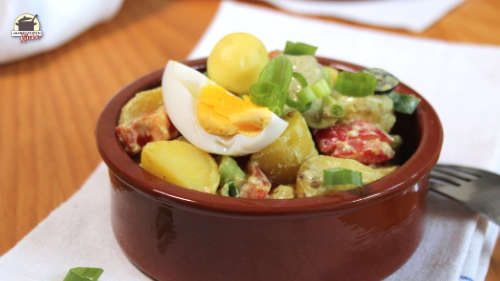 Steingutschale mit Kartoffelsalat, auf dem ein Ei liegt.