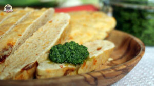 Ein Klacks Petersilien-Pesto auf einem Stück Tomaten-Ciabatta, das auf einem Holzteller liegt.