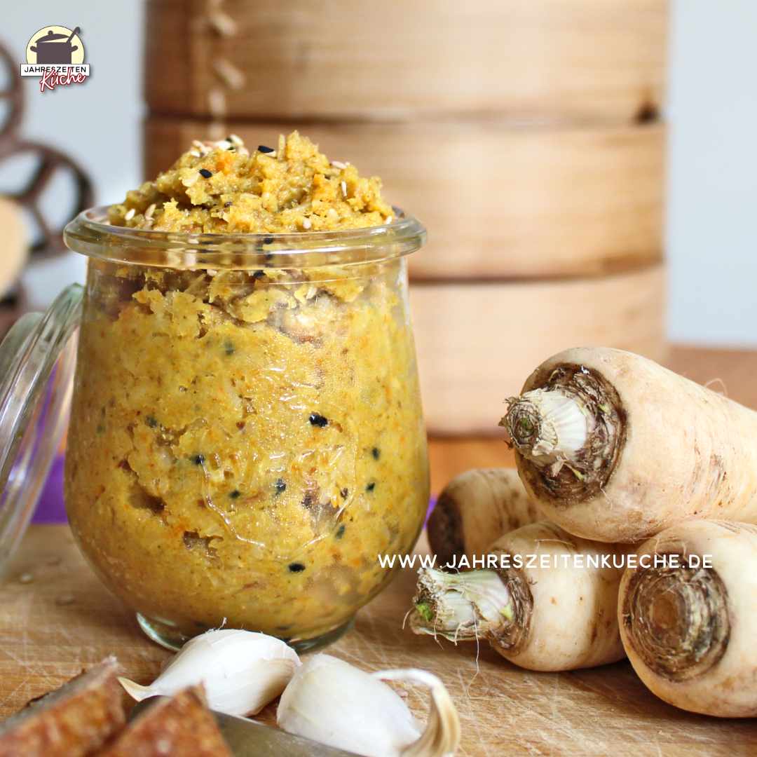 Neben einem Glas Petersilienwurzel-Aufstrich liegen Wurzelpetersilie und Knoblauch.