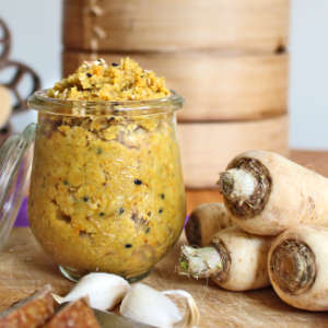 Neben einem Glas Petersilienwurzel-Aufstrich liegen Wurzelpetersilie und Knoblauch.