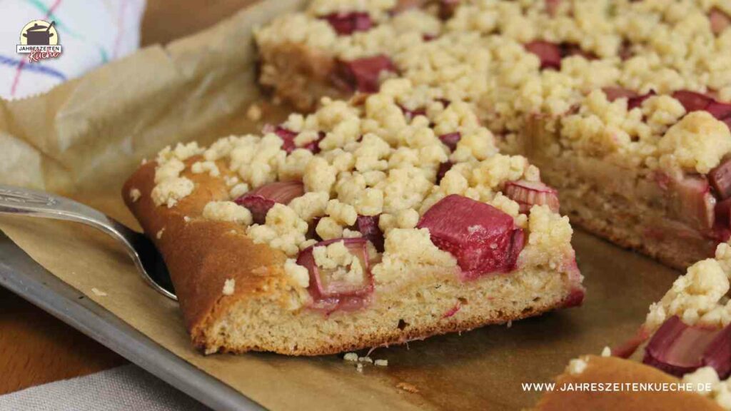 Ein Stück Rhabarberkuchen mit Zimtstreusel liegt auf einem Backblech.