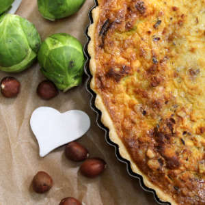 Neben einer Rosenkohl-Quiche liegen Haselnüsse, frischer Rosenkohl und ein kleines Herz.