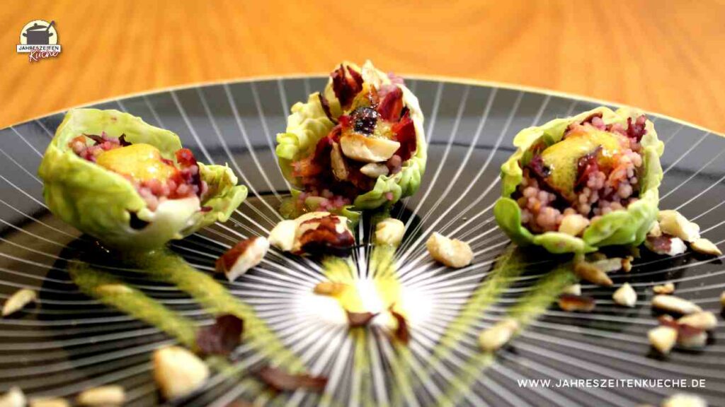 Auf einem schwarzen Teller liegen drei gefüllte Rosenkohlblätter als Fingerfood