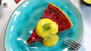 Auf einem ovalen Teller liegt ein Stück Rote-Beete-Quiche. Darauf Joghurtsauce mit Dill.