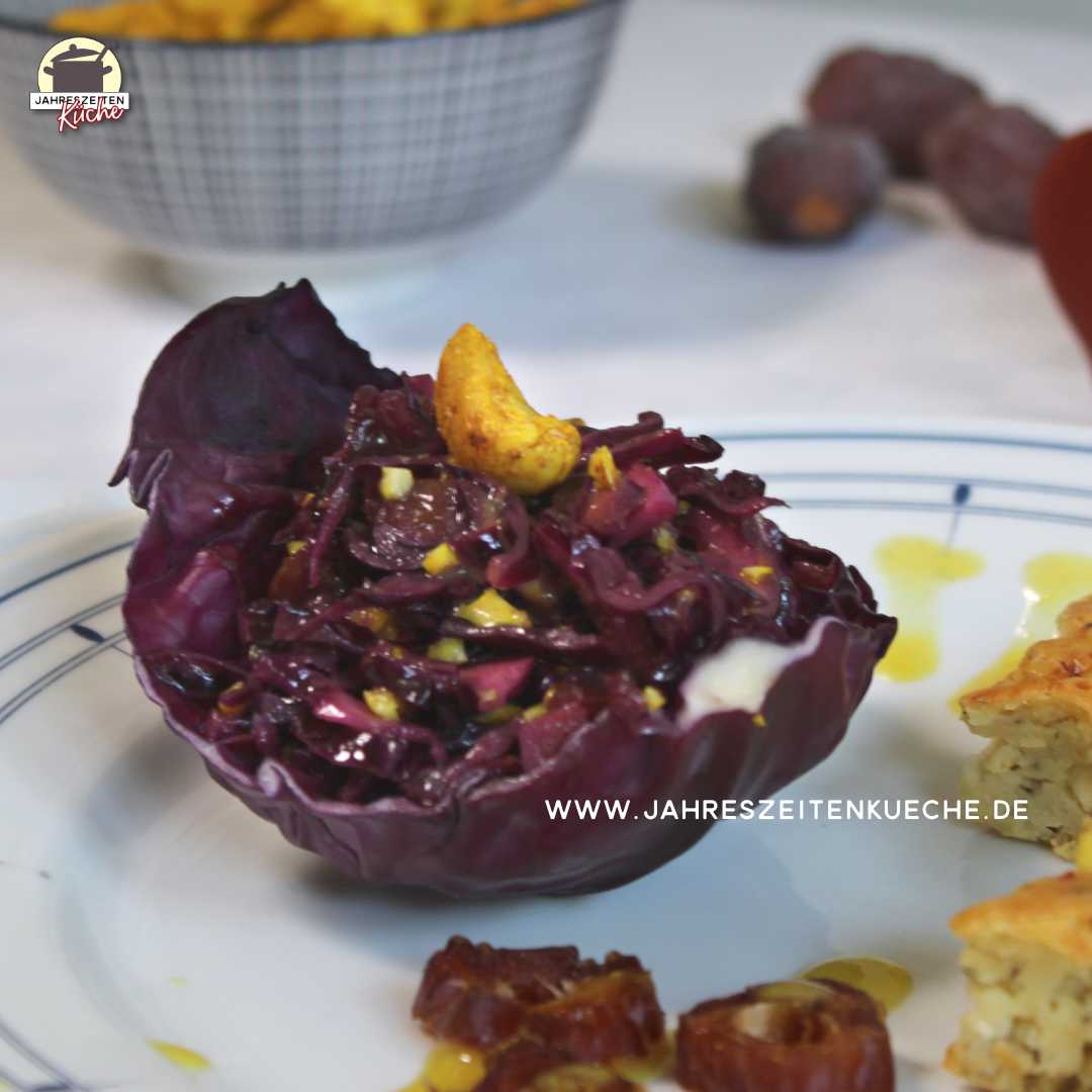 Auf einem Teller liegt ein Rotkohlblatt, in dem Rotkohlsalat mit Cashewkernen angerichtet ist.