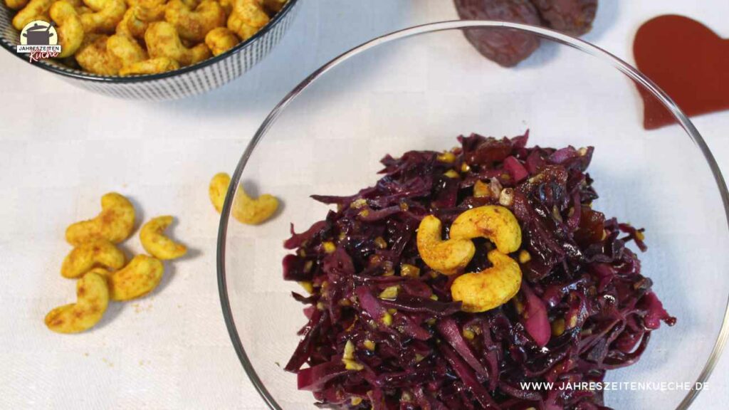 Eine Glasschlüssel mit Rotkohlsalat auf dem 3 Cashewkerne angerichtet sind.