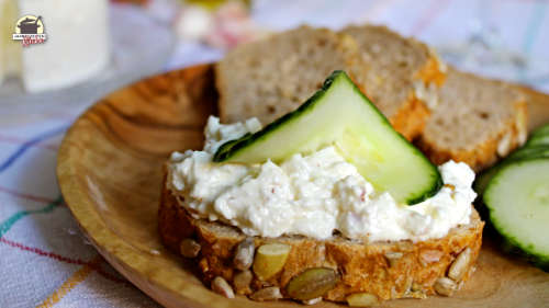 Schafskäsecreme mit Knoblauch auf einem Brot, das mit Gurke garniert ist