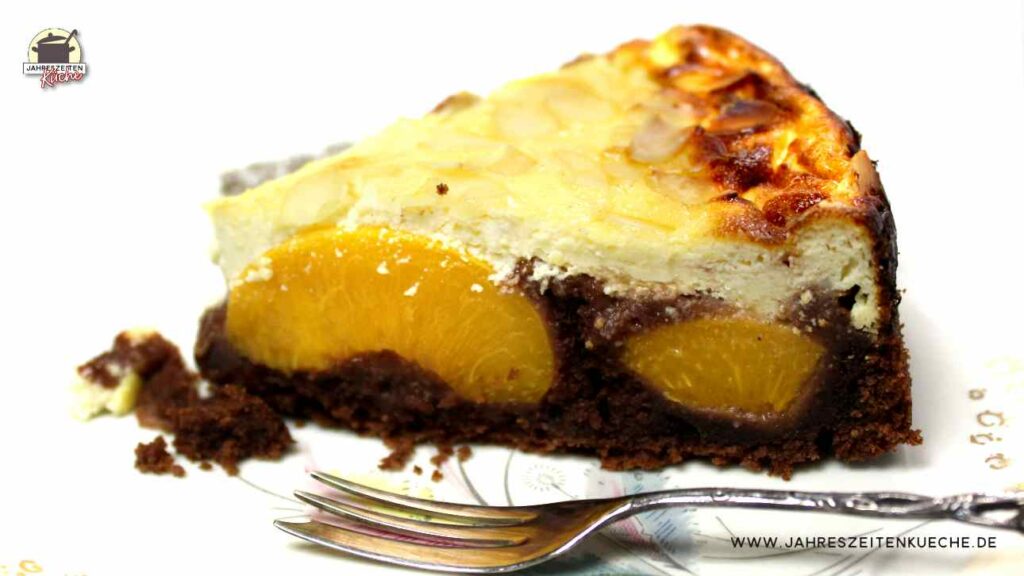 Ein Stück Schokokuchen mit Pfirsich und Käsekuchendecke liegt auf einem Teller. Davor liegt eine Kuchengabel.