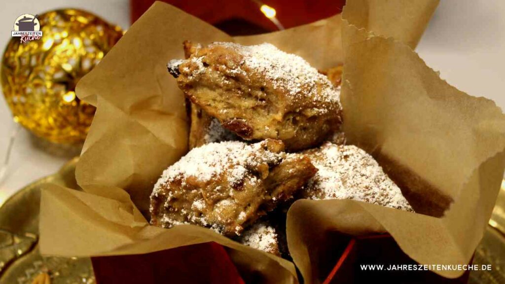 Stollenkonfekt mit Marzipan ist einer roten Dose. Im Hintergrund sind kleine Lichter und eine goldene Kugel
