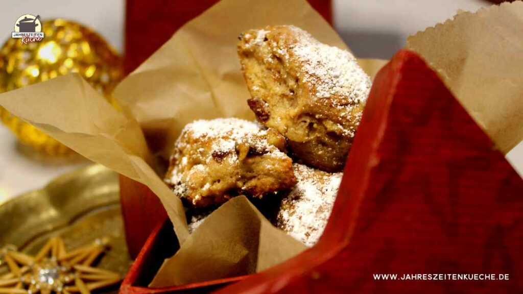 In einer roten Dose ist Stollenkonfekt mit Marzipan. Im Hintergrund liegt eine goldene Kugel