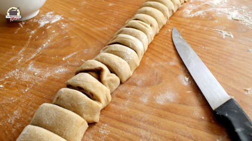 Der aufgerollte Teig ist in Scheiben geschnitten. Daneben liegt ein langes Messer.