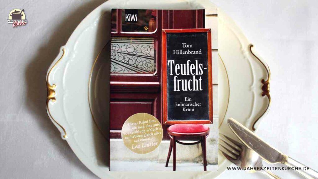 Tom Hillenbrands Buch Teufelsfrucht liegt auf einem weißen Teller mit Goldrand. Daneben liegt Besteck.