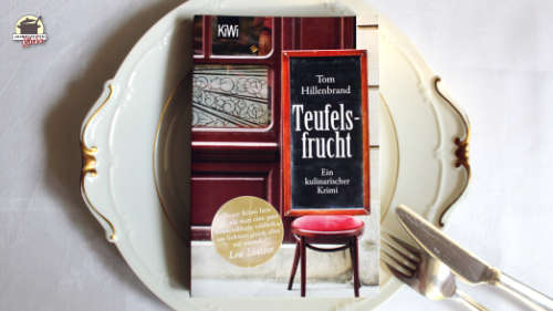 Das Buch Teufelsfrucht liegt auf einem weißen Teller mit Goldrand.