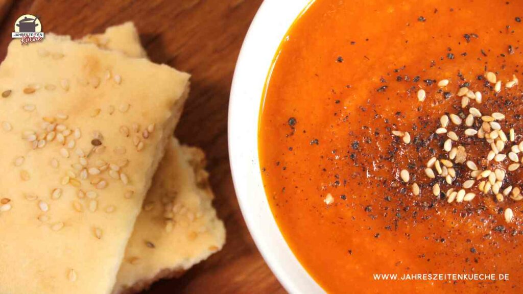 Eine weiße Suppenschale mit Karotten-Tomaten-Suppe. Links daneben liegt Lavashbrot.