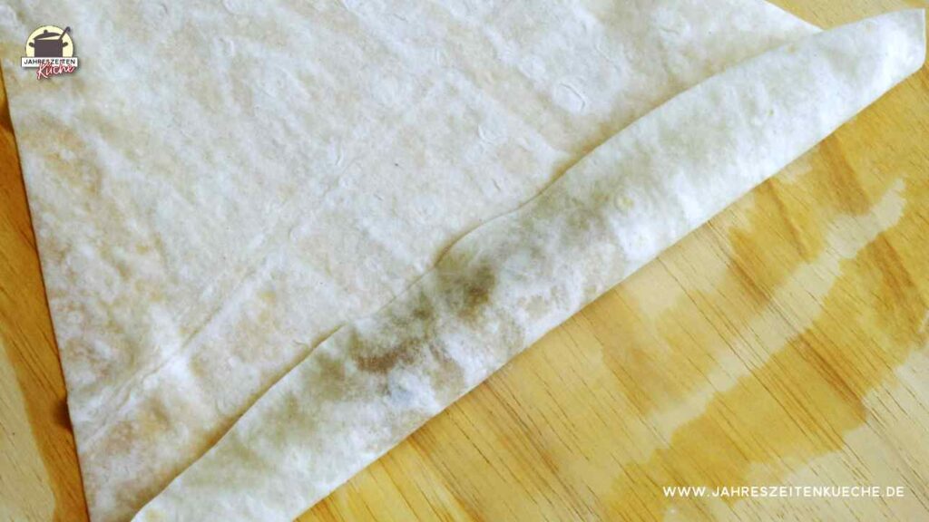 Auf einem Holzbrett liegt Jufkateig, dessen untere Kante umgeklappt ist.