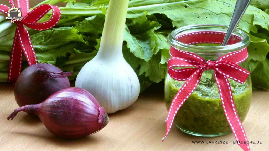 Ein Glas Mairübchenpesto, rote Zwiebeln, Knoblauch sowie ein Bund Mairübchen liegen daneben