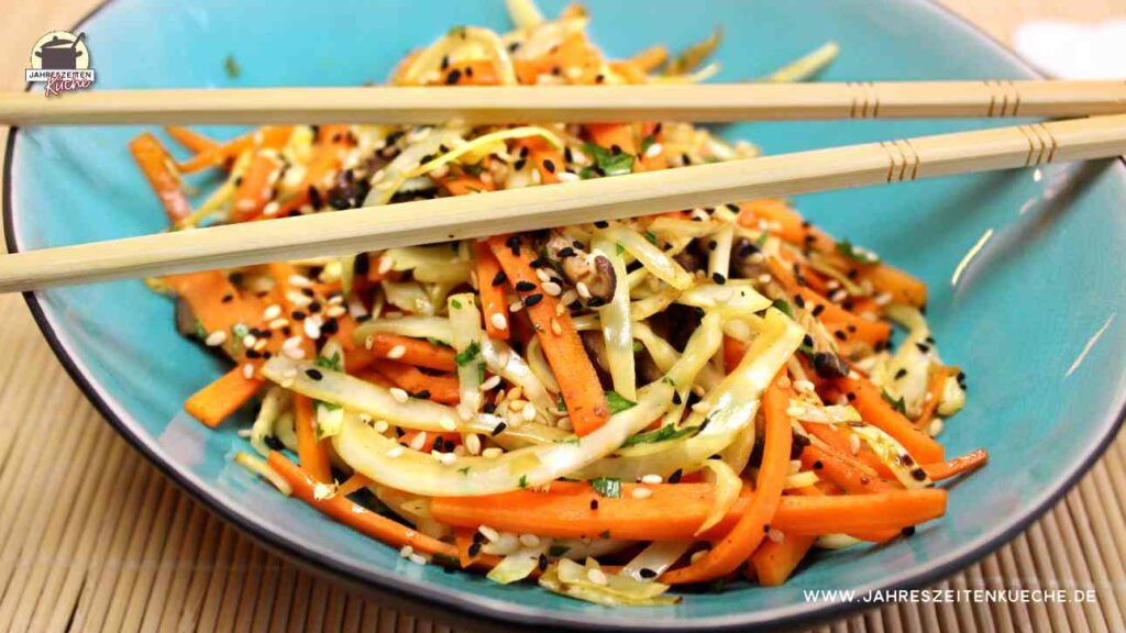 In einer türkisfarbenen Schüssel sind Karotten, Weißkohl und Shiitakepilze aus dem Wok angerichtet. Darüber liegt ein paar Essstäbchen.