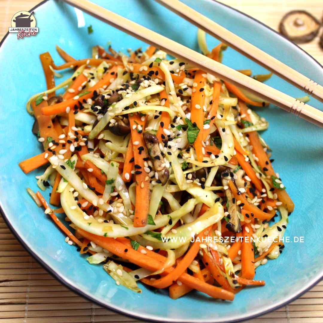 Karotten, Weißkohl und Shiitakepilze aus dem Wok sind in einer ovalen Schale angerichtet. Darüber liegt ein paar Essstäbchen.