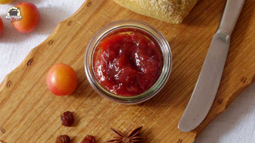 Auf einem Holzbrett liegt ein Messer und daneben steht ein Glas Wildpflaumen-Rosinen-Marmelade mit Sternanis