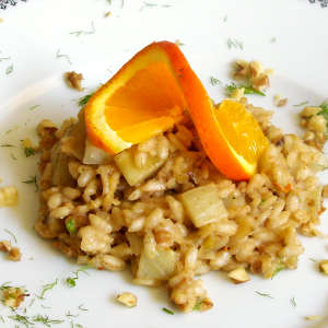 Eine Portion Fenchel-Walnuss-Risotto ist auf einem weißen Teller mit einer Orangensacheibe angerichtet.