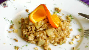 Ein weißer Teller mit Winterrisotto, das mit einer gedrehten Orangenscheibe garniert ist.