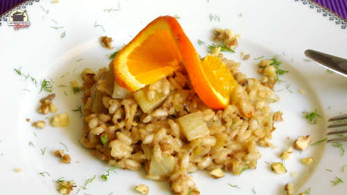 Ein weißer Teller mit Winterrisotto, das mit einer gedrehten Orangenscheibe garniert ist.