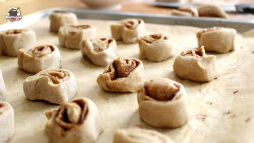 Aufgerollte Zimtschnecken liegen auf einem mit Backpapier ausgelegtem Backblech.