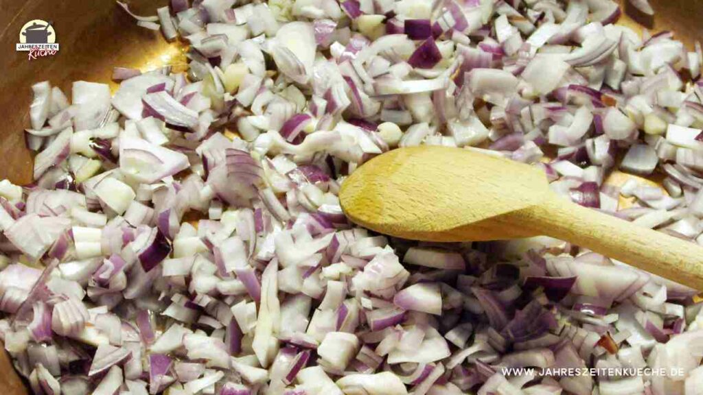 Frische Zwiebeln mit Holzlöffel in einem Kupfertopf