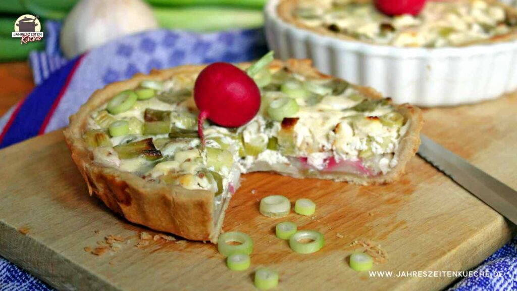 Eine angeschnittene Zwiebelquiche liegt auf einem Holzbrett.