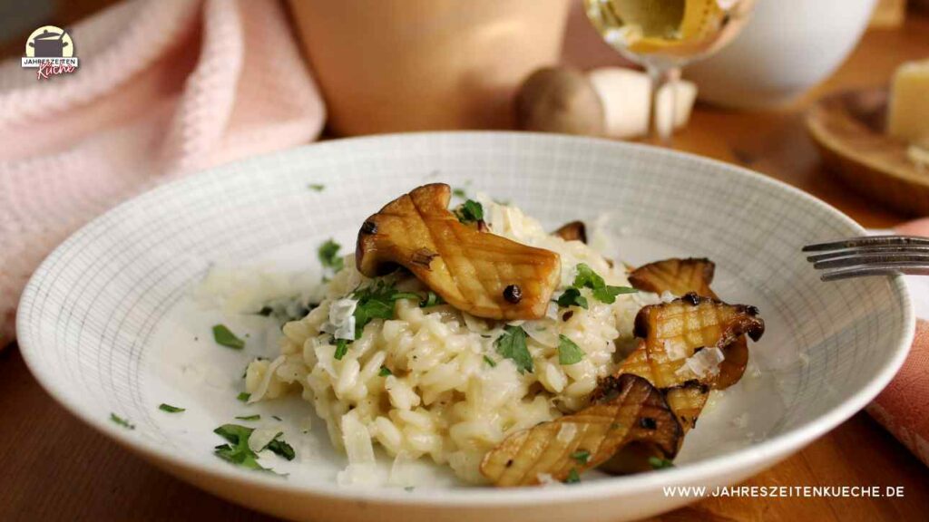 Ein Teller mit Käruterseitling-Risotto. Im Hintergrund steht ein Glas Weißwein.