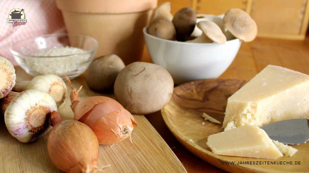 Kräuterseitlinge, Zwiebeln, frischer Knoblauch, Parmesan und Risottoreis auf einem Holztisch