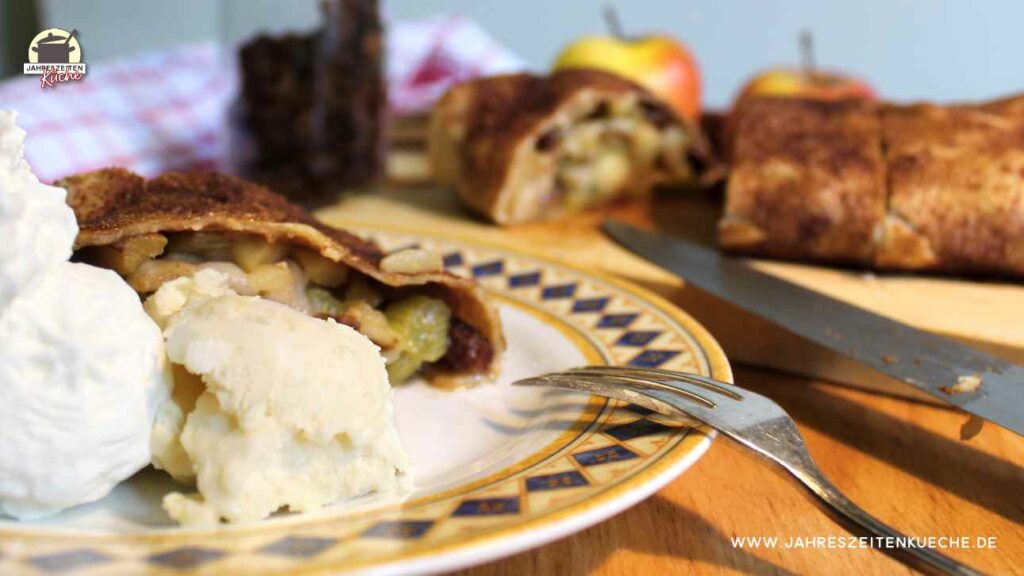 Ein Stück Apfel-Rhabarber-Strudel mit Vanilleeis und Sahne liegt auf einem Porzellanteller