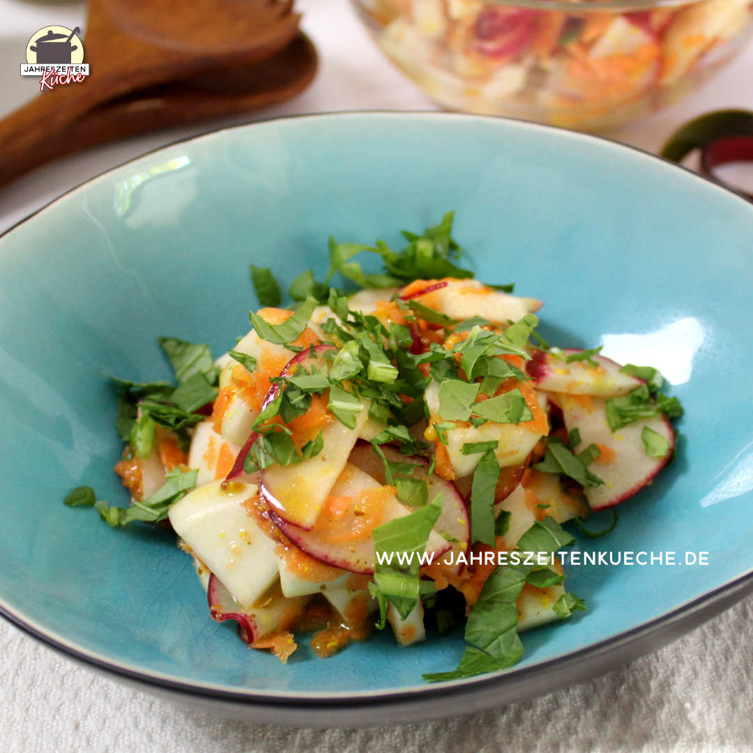 In einer türkisfarbenen Bowl ist eine Portion Mairübchen-Salat mit Grün bestreut. In Hintergrund liegt ein Salatbesteck aus Holz.