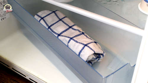 Ein zusammengerolltes Geschirttuch liegt in der Gemüseschale des Kühlschranks