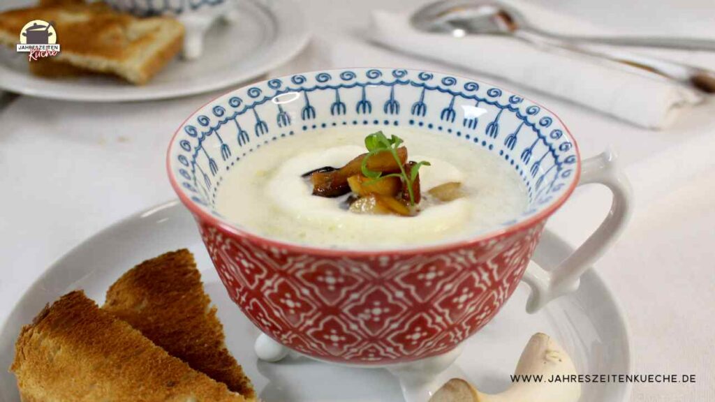 In einer Tasse ist eine Portion Spargelcremesuppe mit Kräuterseitlingen. Daneben liegen Kräuterseitlinge und Toastbrotscheiben