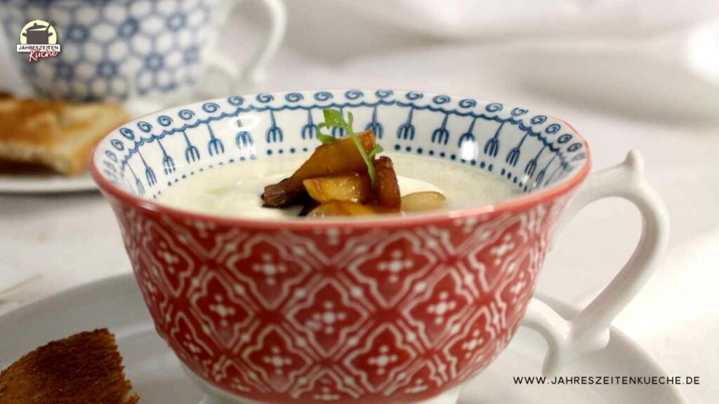 In einer Tasse ist eine Portion Spargelcremesuppe mit Kräuterseitlingen. Daneben liegen Kräuterseitlinge und Toastbrotscheiben