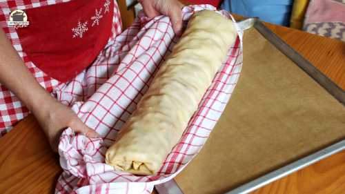 Aufgerollter Strudel wird mithilfe eines Leinentuchs auf ein Backblech gehoben