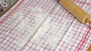 Leinentuch ist mit Mehl bestäubt. Darauf liegt eine Teigrolle aus Holz