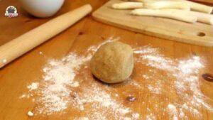 Eine Teigkugel liegt auf einer bemehlten Tischplatte neben einem Teigroller.