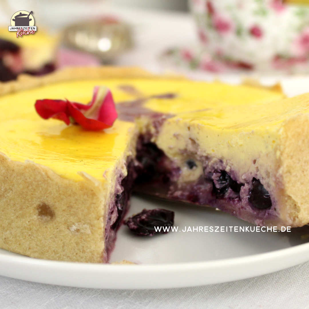 Ein angeschnittener Heidelbeer-Käsekuchen liegt auf einem weißen Teller.