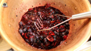 In einem Konfitüretopf steht ein Kartoffelstampfer zum Zerkleinern der Beeren und Kirschen.