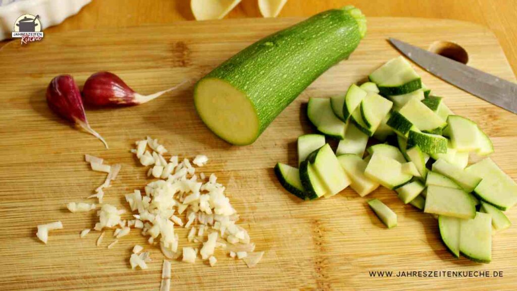Auf einem Holzbrett ligen geschnitten Zucchini und fein gehackter Knoblauch.