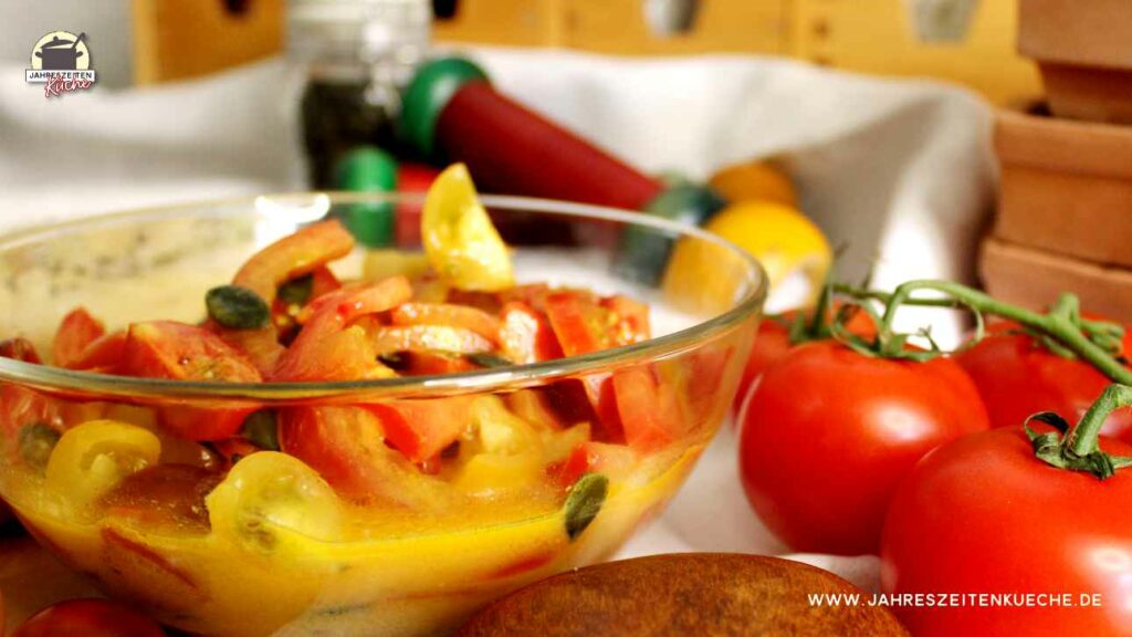 Neben einer Schüssel Tomatensalat mit Senfdressing liegen frische Strauchtomaten