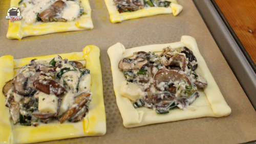 Mit Champignon und Frühlingszwiebeln gefüllter Blätterteig liegt auf einem Backblech